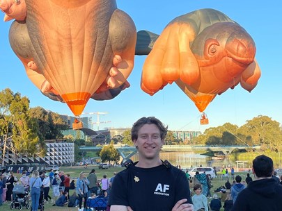 Connor Jolly standing in a park with animal-shaped hot air balloons floating behind him
