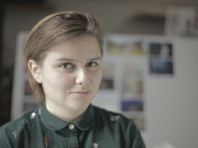 Headshot of Clemence smiling with an out-of-focus gallery of artwork behind them