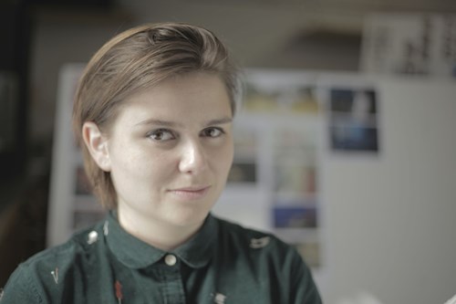 Headshot of Clemence smiling with an out-of-focus gallery of artwork behind them