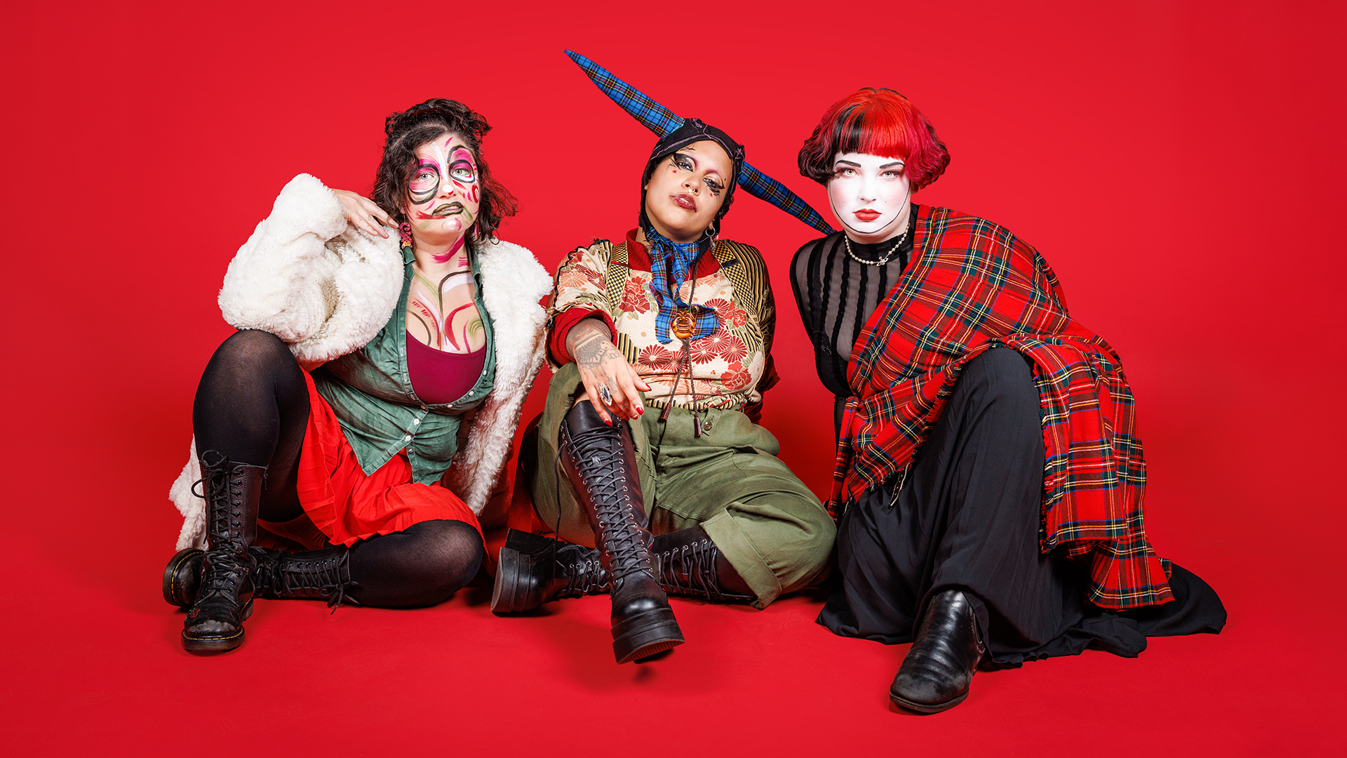 Three people against a vibrant red background wearing colourful red-hue clothing