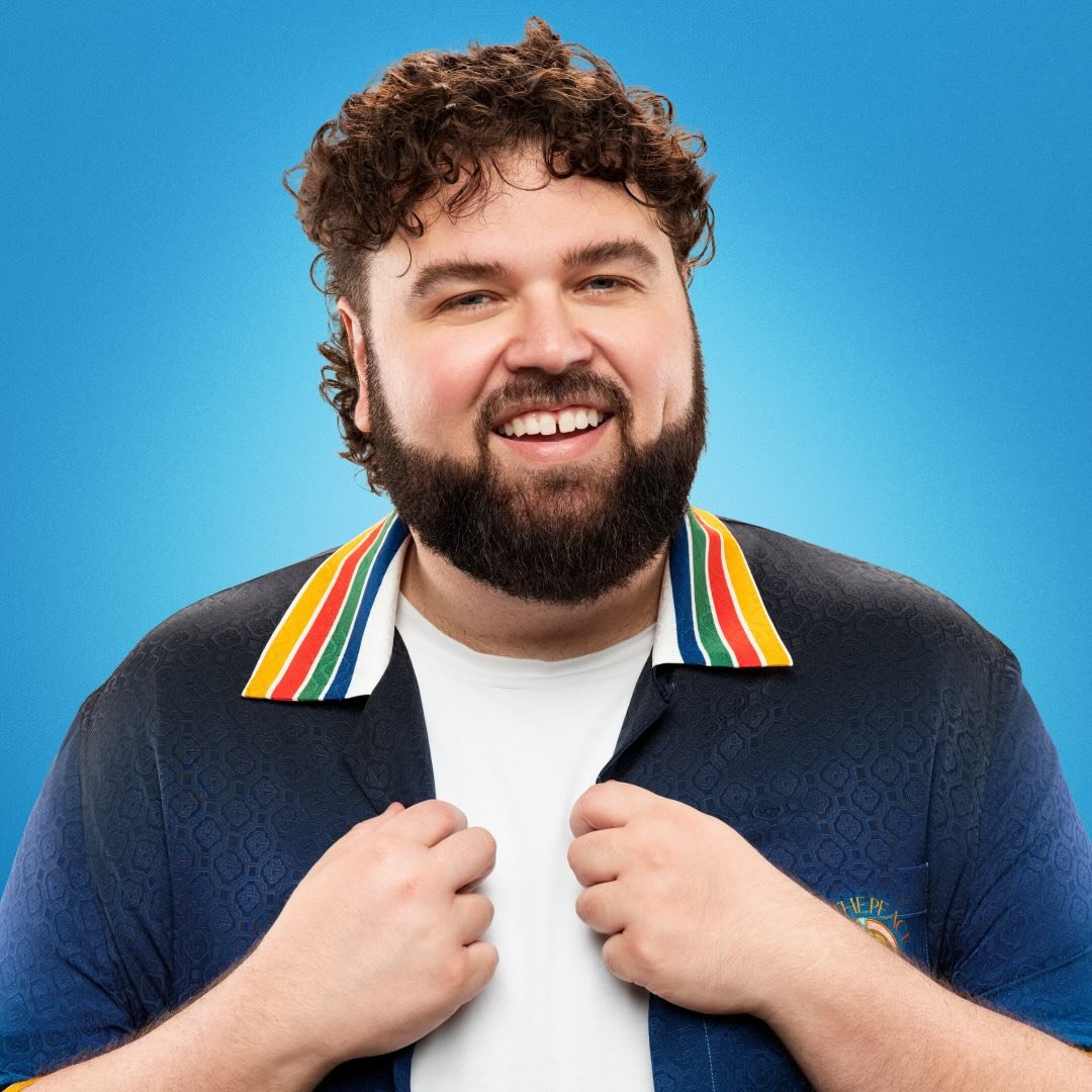 Headshot of Chris Demos looking rather pleased with themselves while holding their hands in front of their chest