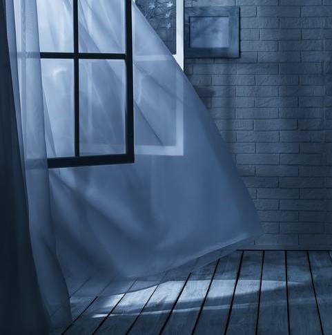 An empty window lit in blue (night-like) lighting, window open, with wind blowing the curtains
