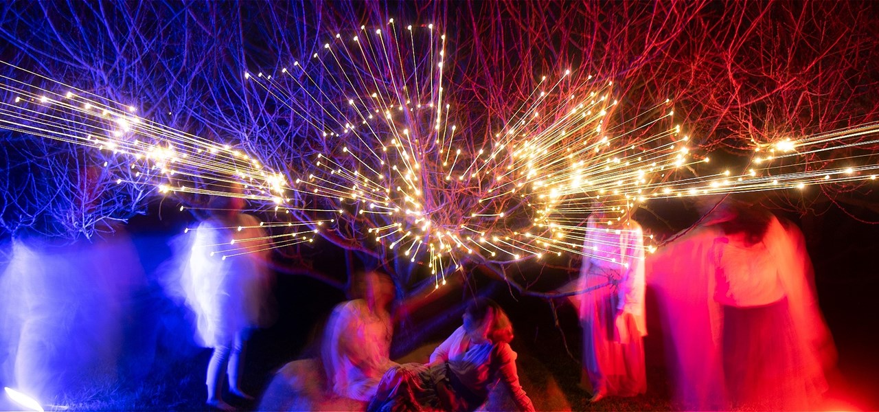 Image by Greta Bernard - a multi-exposure picture taken at night of people swirling a hand-held light