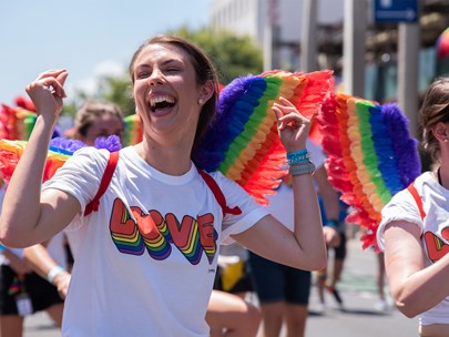 Group of marchers at Pride March looking very happy, wearing t-shirts that say 'Love' and sprouting large, rainbow wings