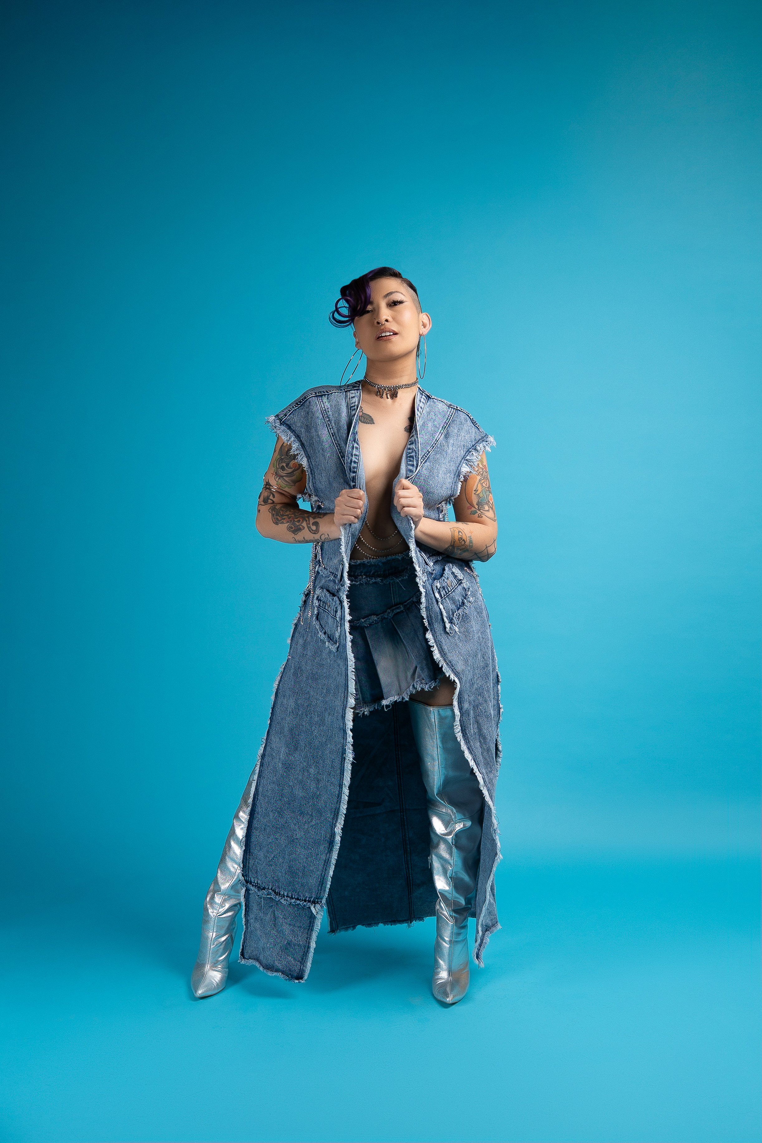 Dominica dressed in denim and shiny long-leg boots against a blue background