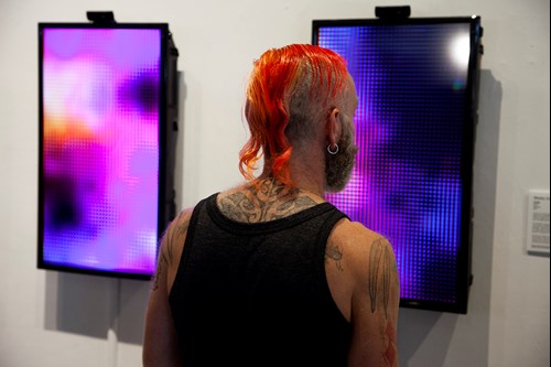 Person staring intently at one of two digital screens hanging on wall as pieces of art