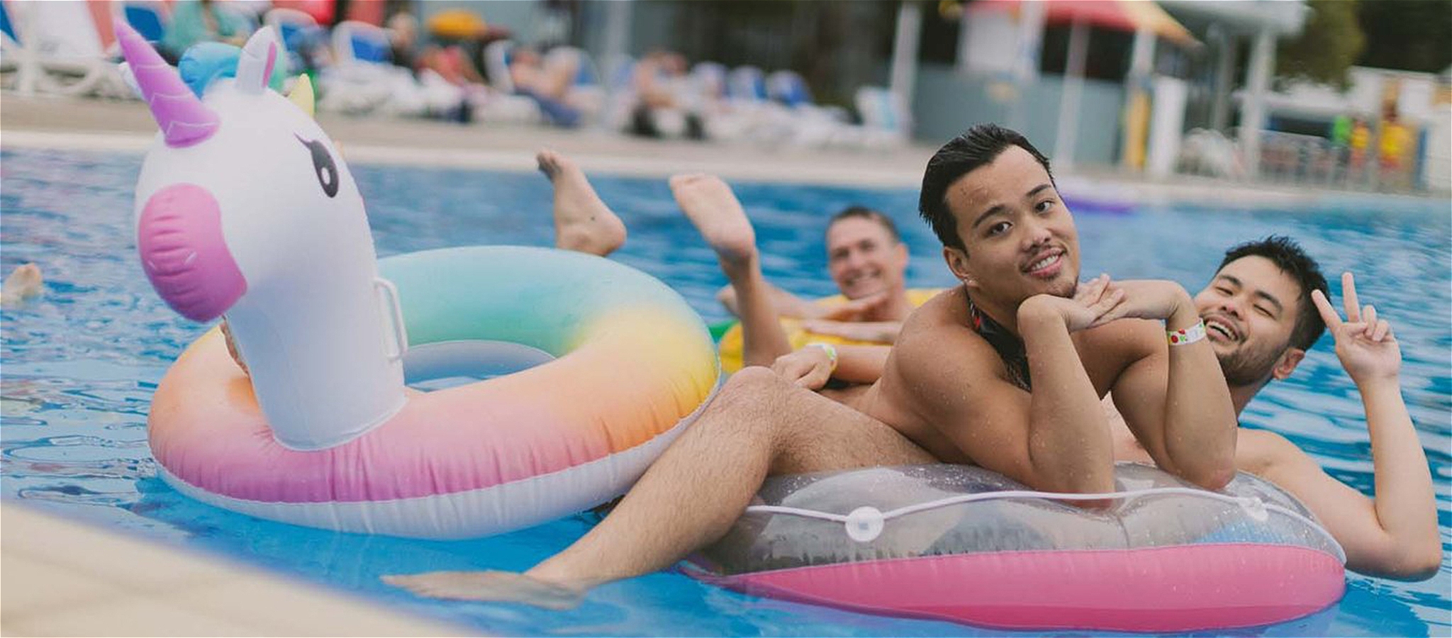 Three people smiling and posing while laying on top of unicorn floaties in the pool.