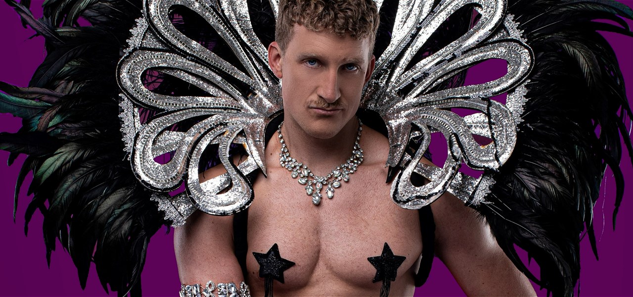 Ziegfeld Boy faces the camera wearing a big silver and black feather collar and black nipple pasties.