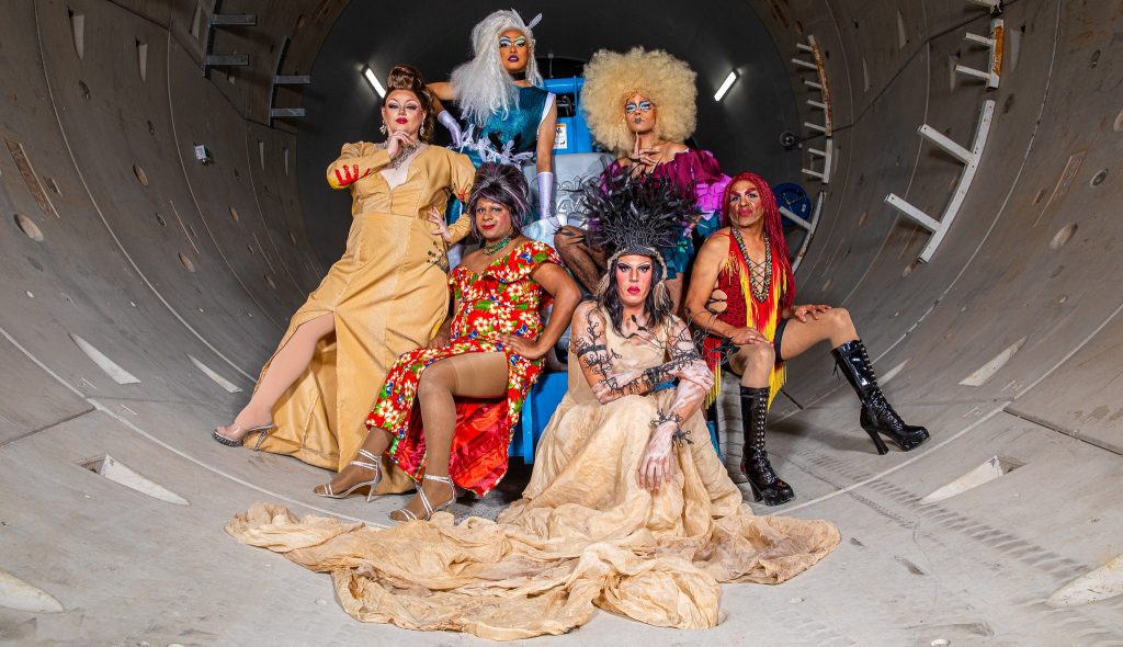 Photo of six glamourously dressed First Nations people inside a large concrete tunnel-like object