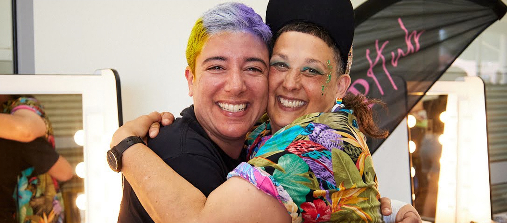 Two individuals smiling at the camera, arms wrapped around each other.