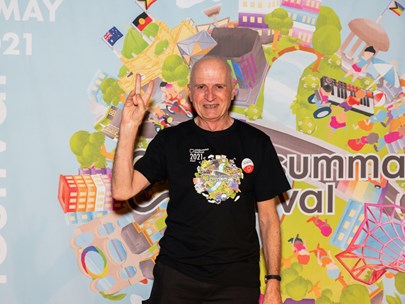 Alan Drummond wearing a 2021 Midsumma t-shirt, standing in front of the 2021 hero image
