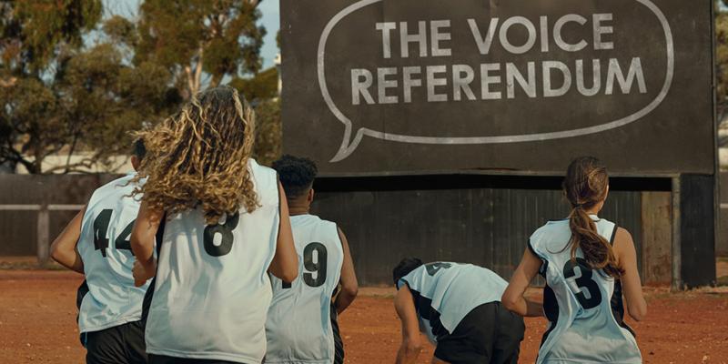 Netball players from behind in outback Australia with a large sign - THE VOICE REFERENDUM