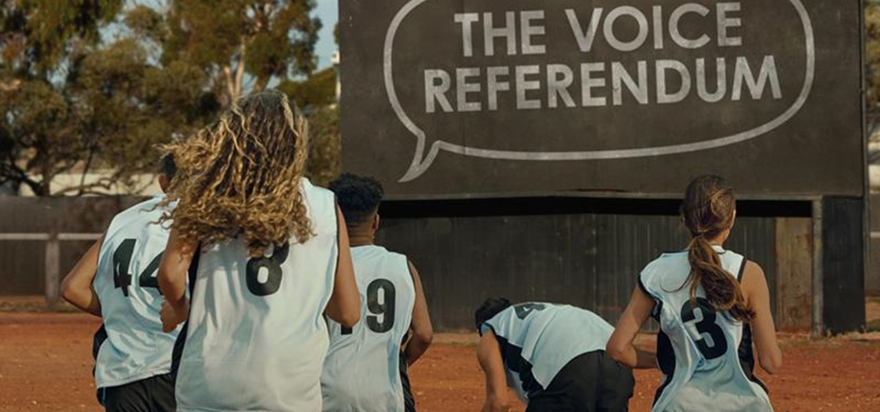 Netball players from behind in outback Australia with a large sign - THE VOICE REFERENDUM