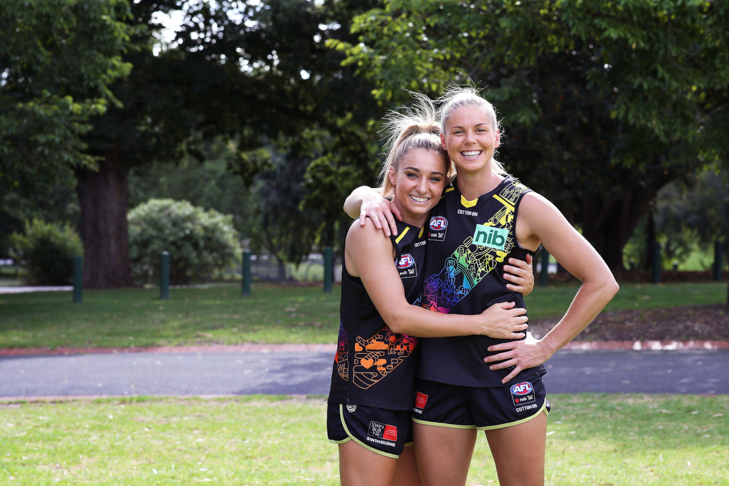 Two female AFL players hugging each other in a public park