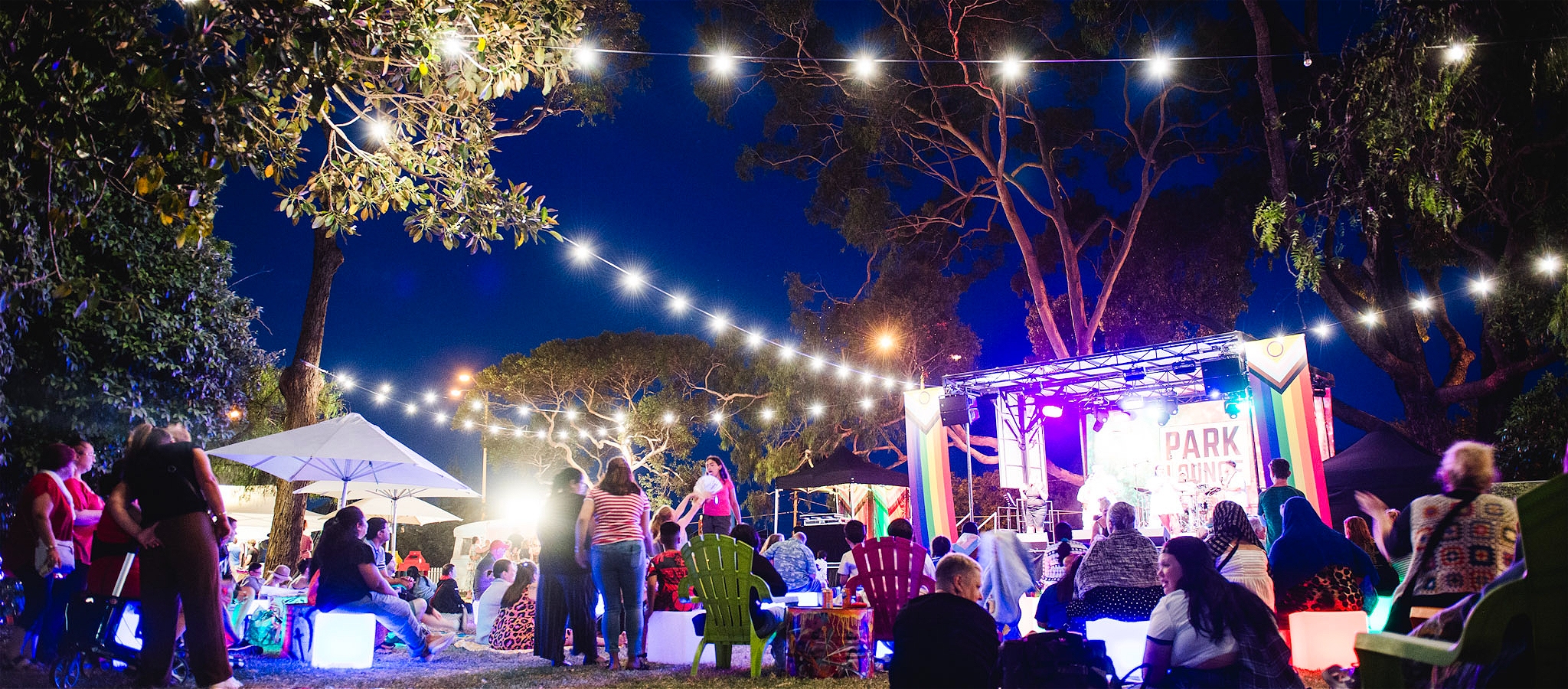 Families and groups Gather in front of the colorful Park Lounge stage, surrounded by trees and festoon lighting
