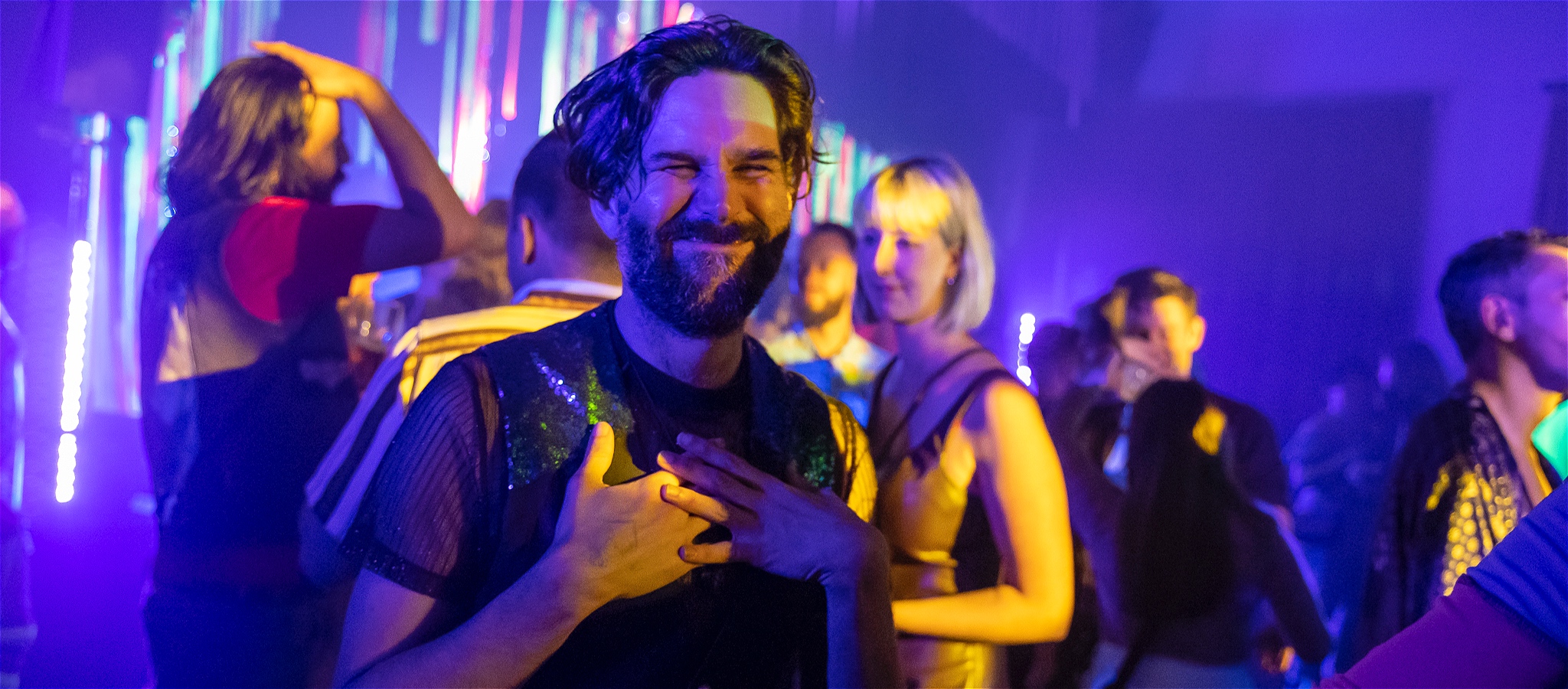 A handsome bearded young man smiling on the dance floor of a black-light venue