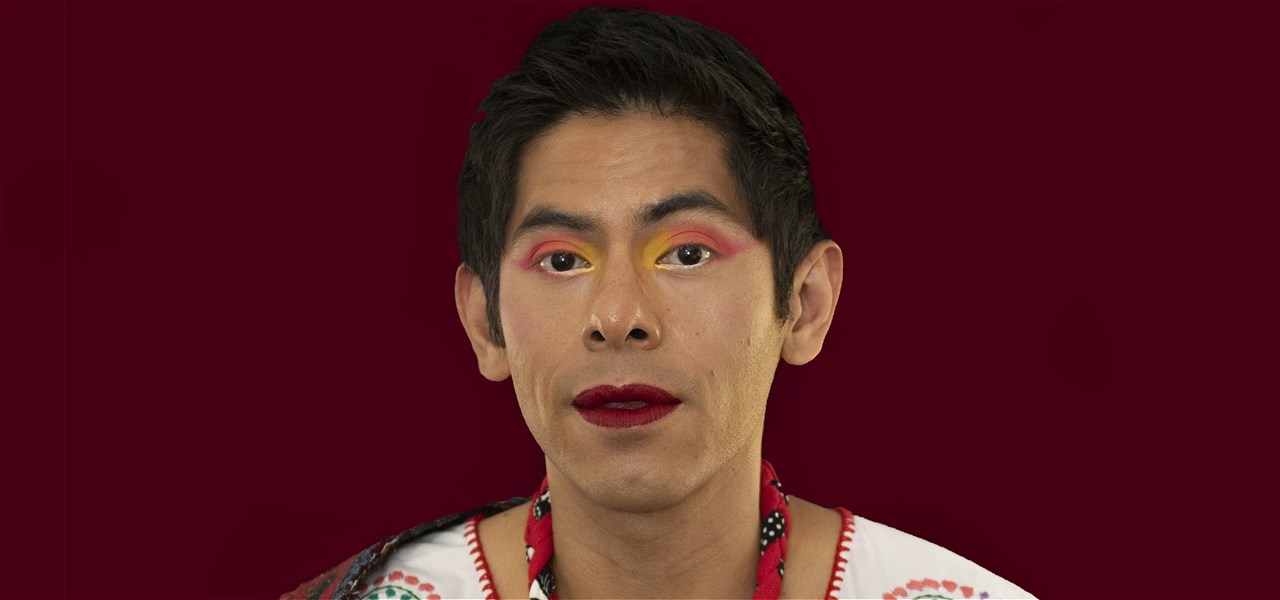 Image of person wearing bright make-up against a maroon background wearing white and floral garments