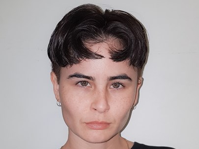 Ellen has high cheekbones and fair skin. They have brown eyes and black hair and pout for the camera. The haircut is very short parted in the middle.
