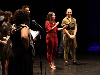 4 actors & 2 playwrights address an audience on stage in a black box theatre; the MC is in the foreground with their back turned to the camera