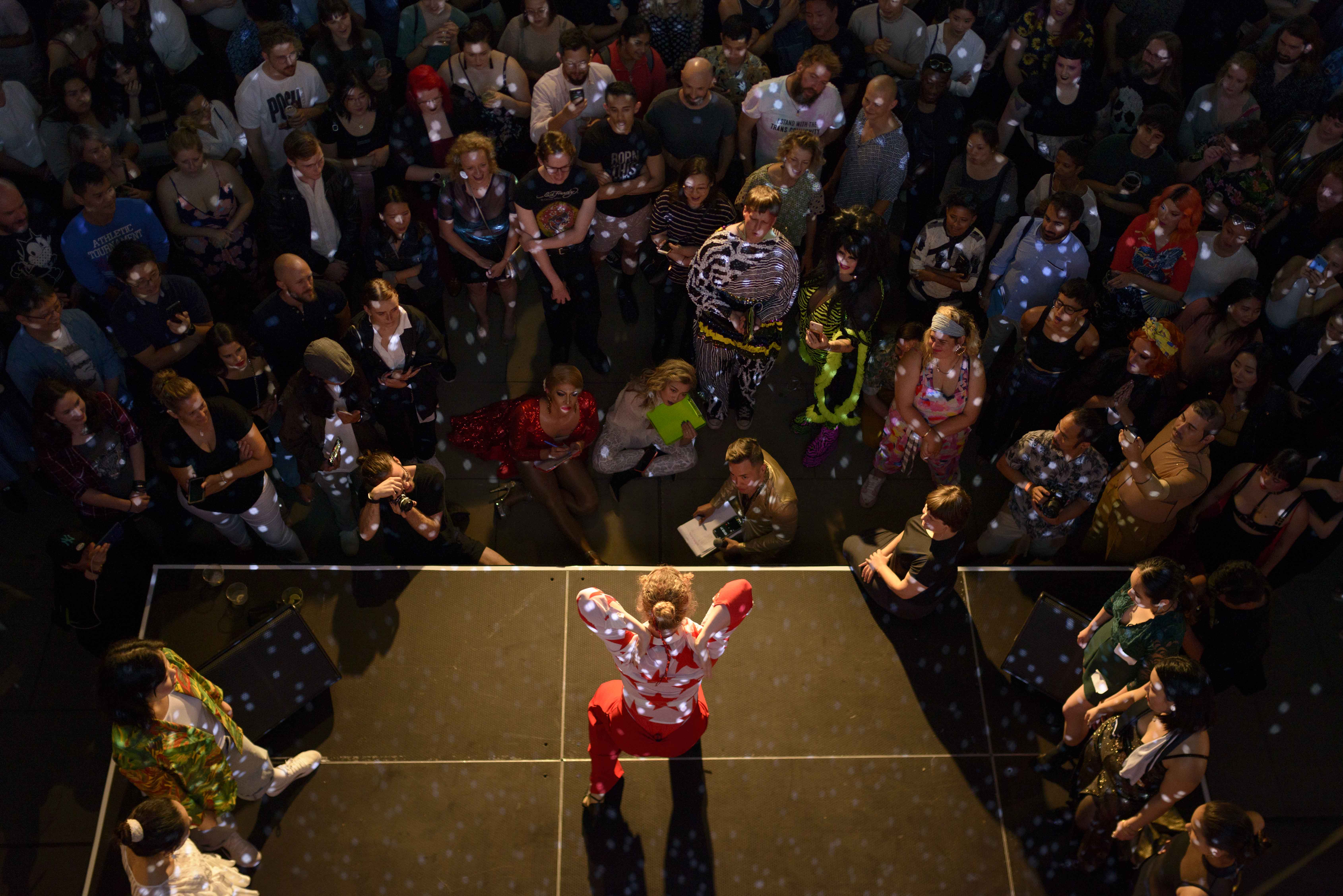 Performer on stage with arms raised and audience all around them