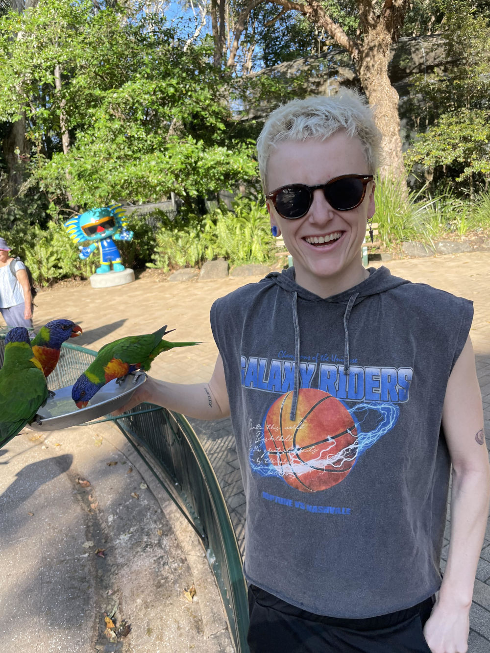 Photo of Helen in a park beside grass parrots eating from a dish they are holding