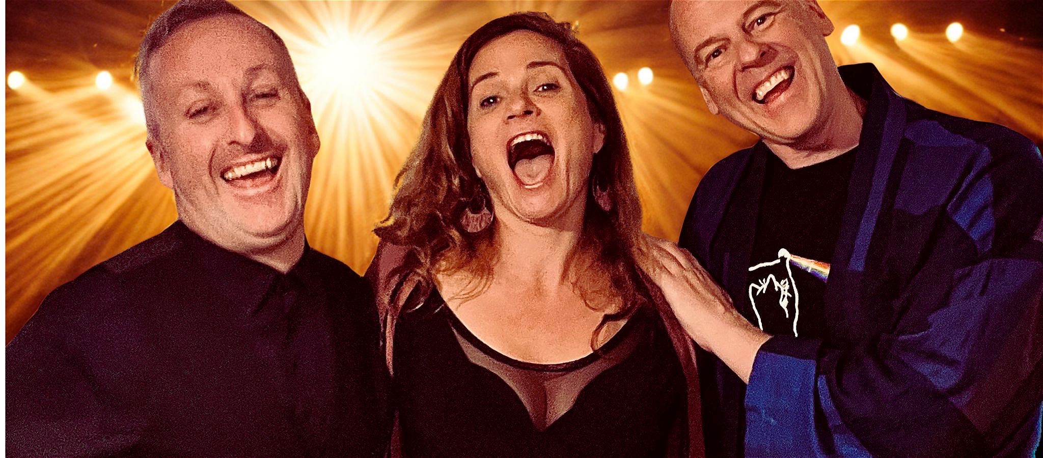 Two men and a woman standing in front of stage lights laughing.