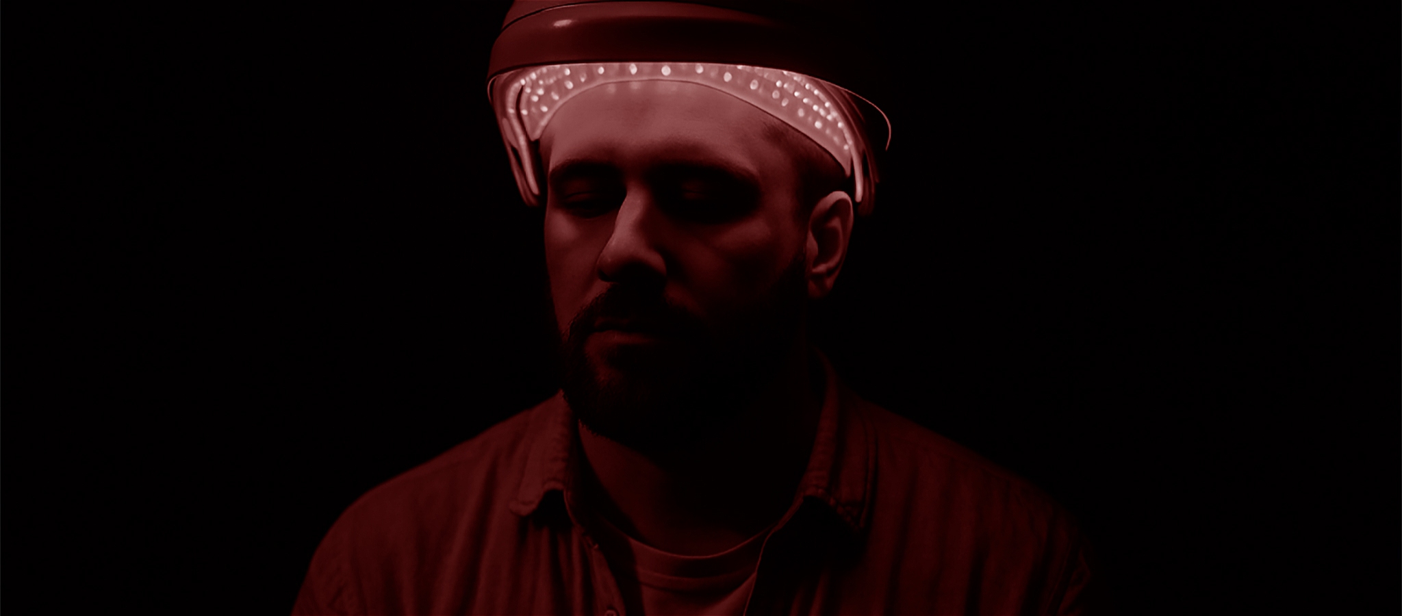 A photograph of a person wearing a hat that lights their face. There is a red glow over the image.
