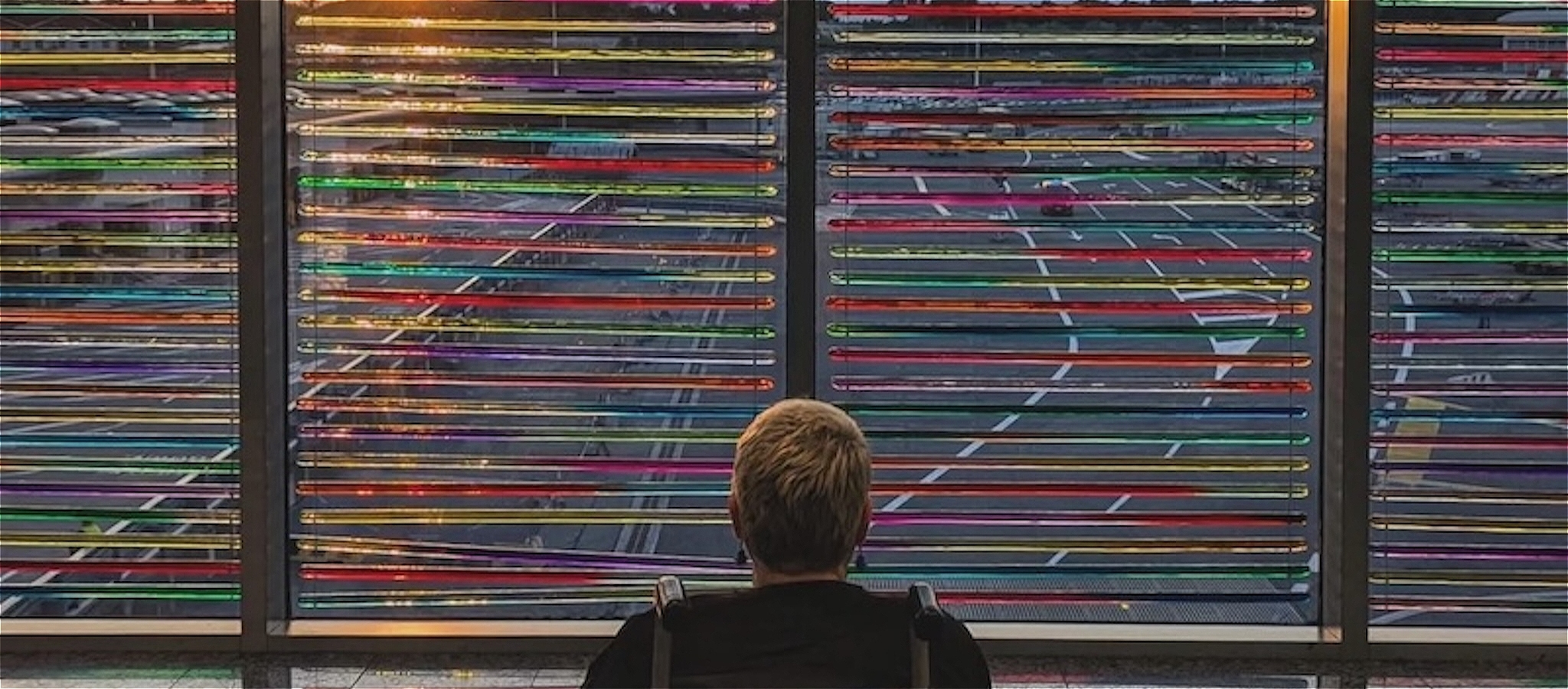 Caroline Bowditch faces the window looking out onto the road with the sun setting through rainbow coloured blinds