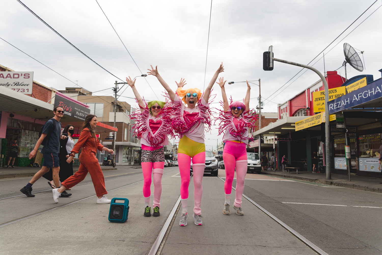 People dressed in outlandish, pinkish costumes dancing on the tram tracks with arms in the air