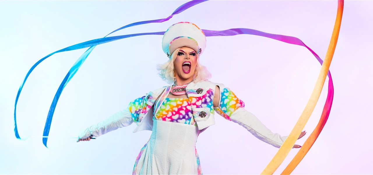 Person dressed in white dress, gloves and hat with rainbow coloured top gaily twirling rainbow ribbons