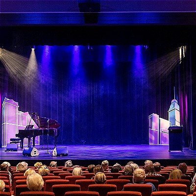 Interior of the main theatre showing audience in foreground and a stage with a grand piano in blue lighting