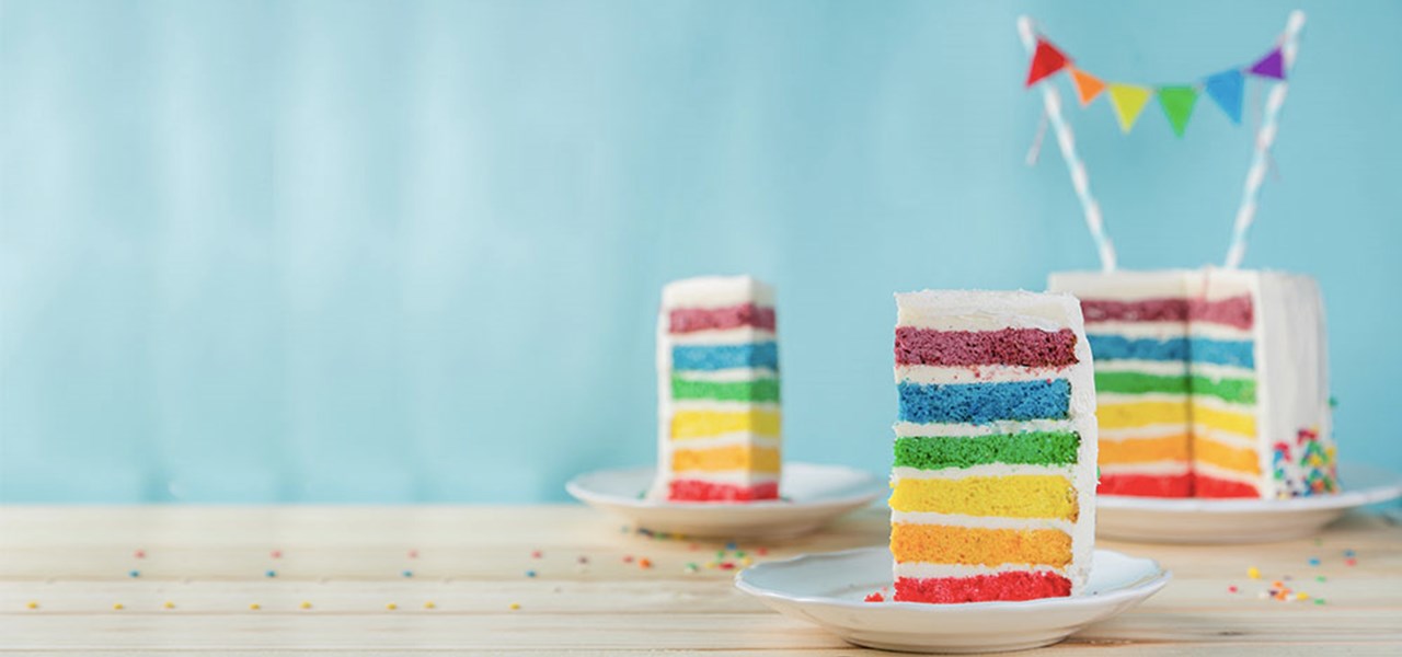 A rainbow layers cake, with two pieces cut out, presented on small plates 