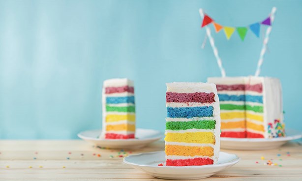 A rainbow layers cake, with two pieces cut out, presented on small plates