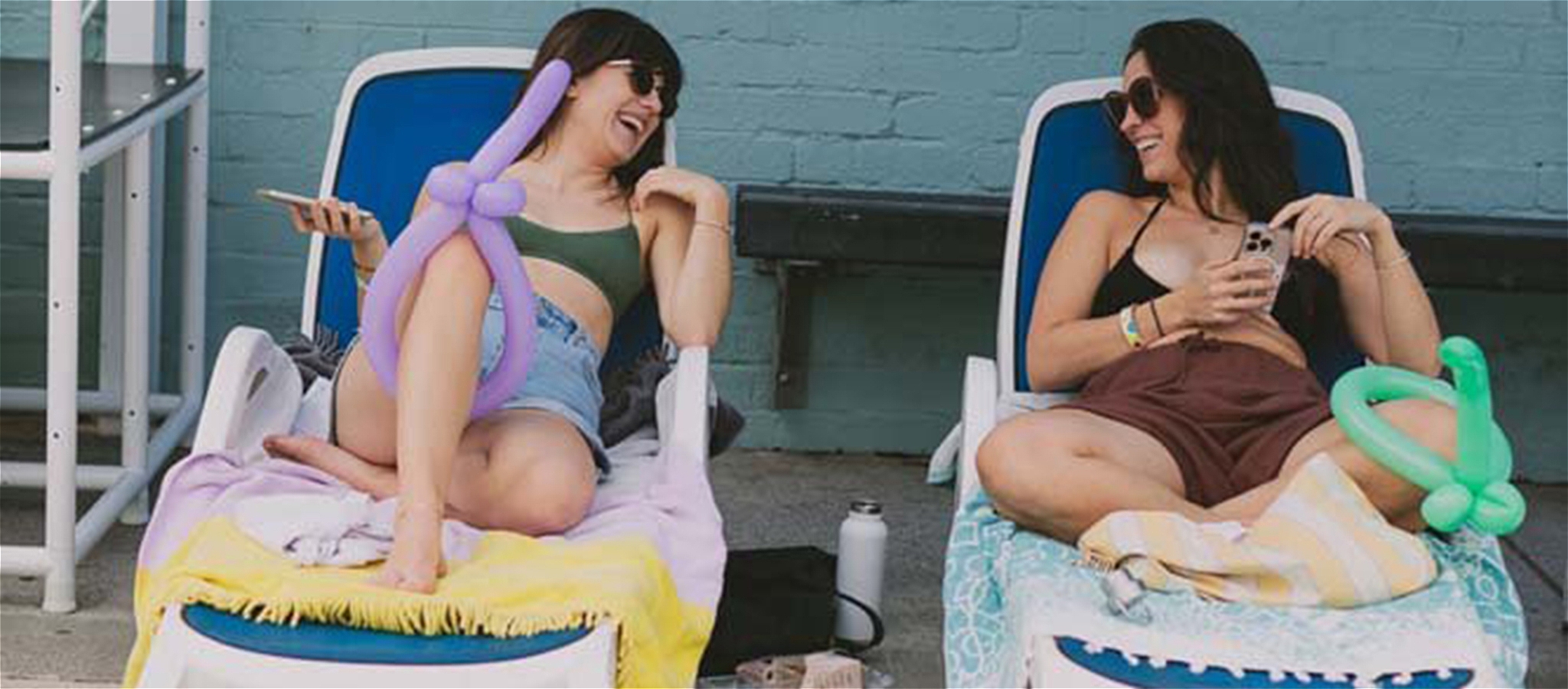 Two people sitting on deck chairs having fun talking to one another with balloons tied around a leg.