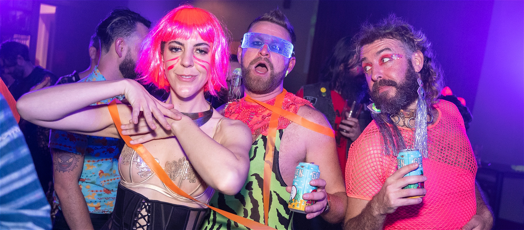 A woman and two men wearing neon outfits dancing on a black lit dance floorA woman and two men wearing neon outfits dancing on a black lit dance floor