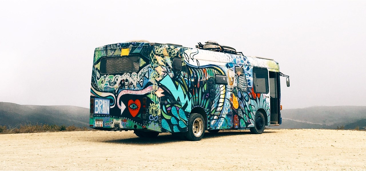 A colourfully decorated bus on a gravel area with hills visible in the background