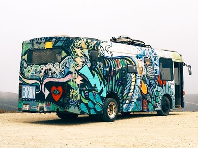 A colourfully decorated bus on a gravel area with hills visible in the background