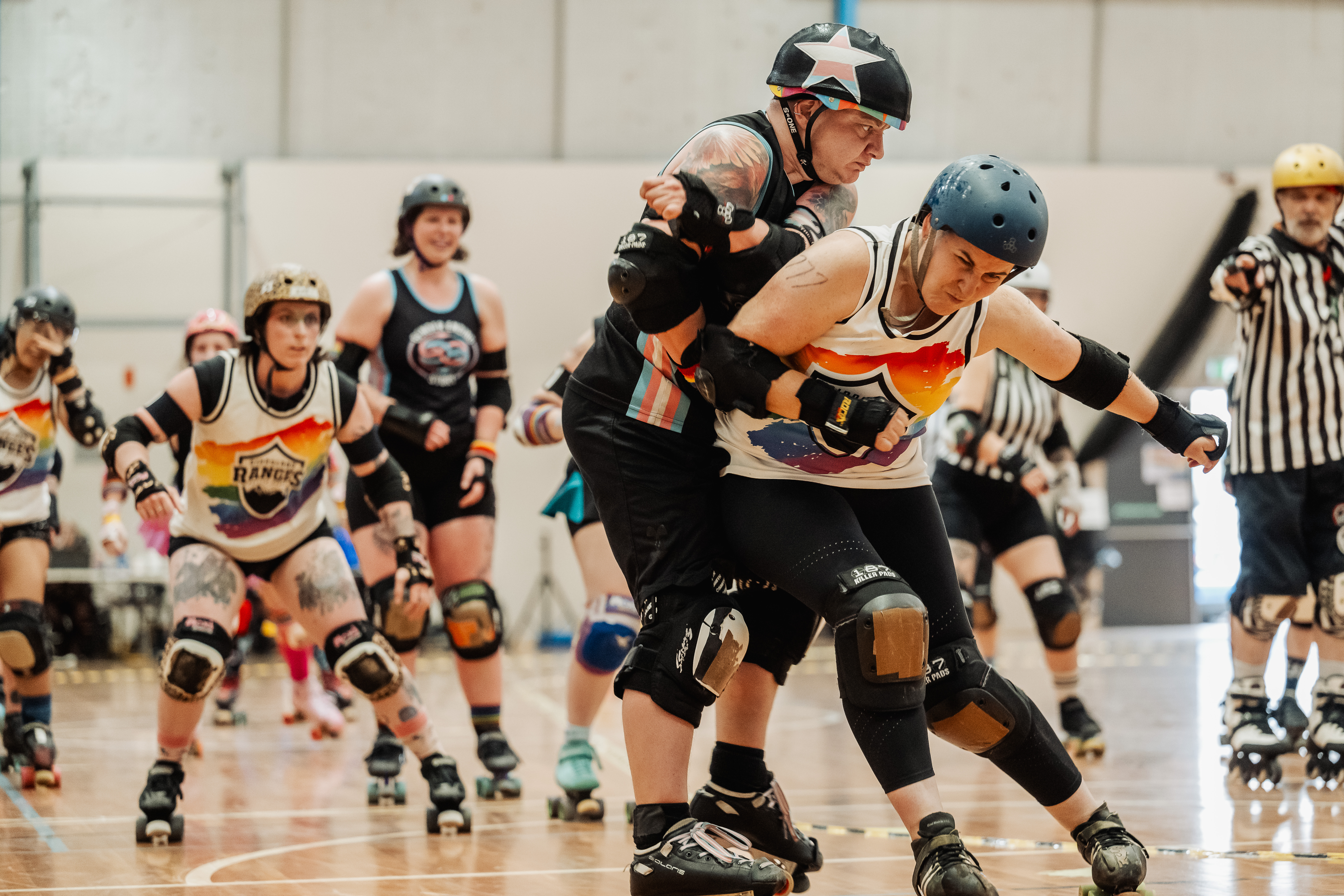 A group of LGBTQIA+ roller derby players and umpires celebrating on the track.