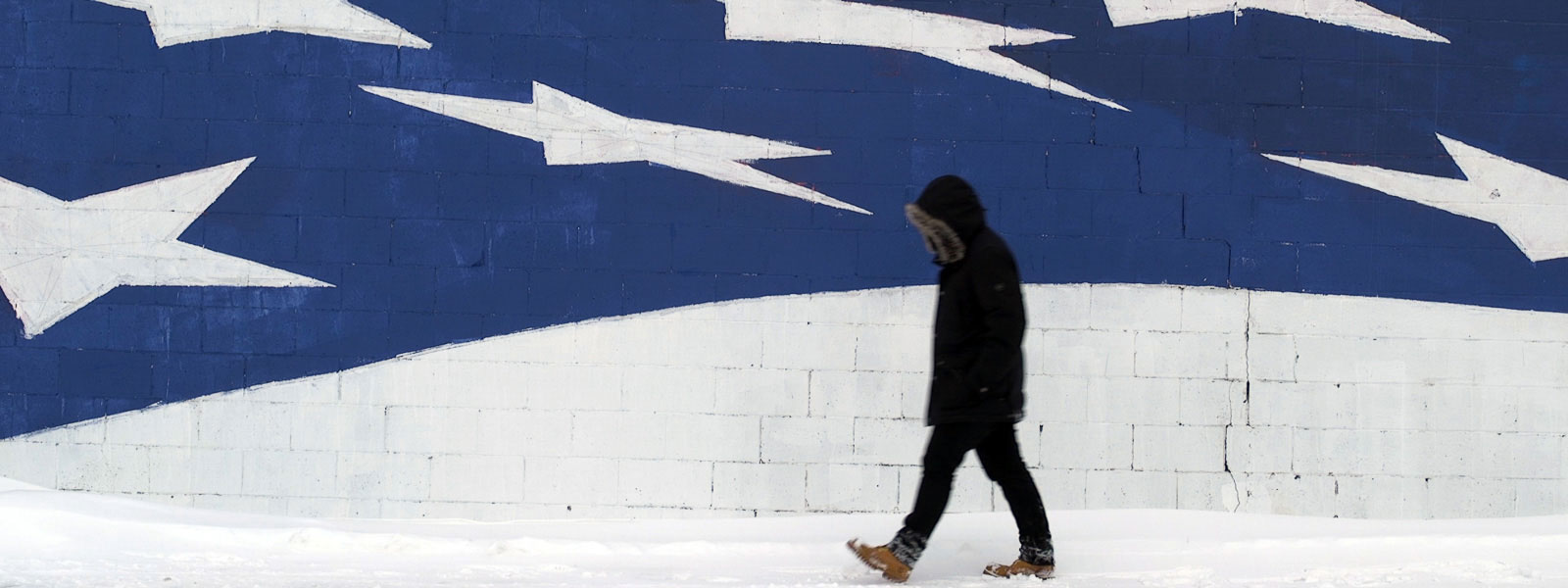A person dressed in black walking, with a wall behind them. The top part of the wall has a blue background and lots of white stars.