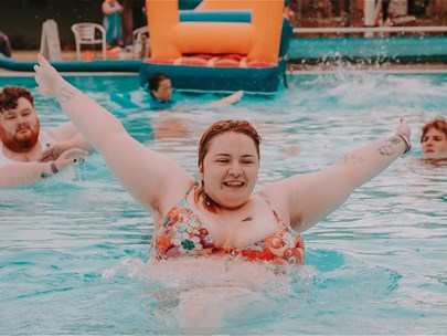 Several young people having fun in the pool at the Pride Pool Party in Sunshine event last year. One of them is leaping out of the water with a smile