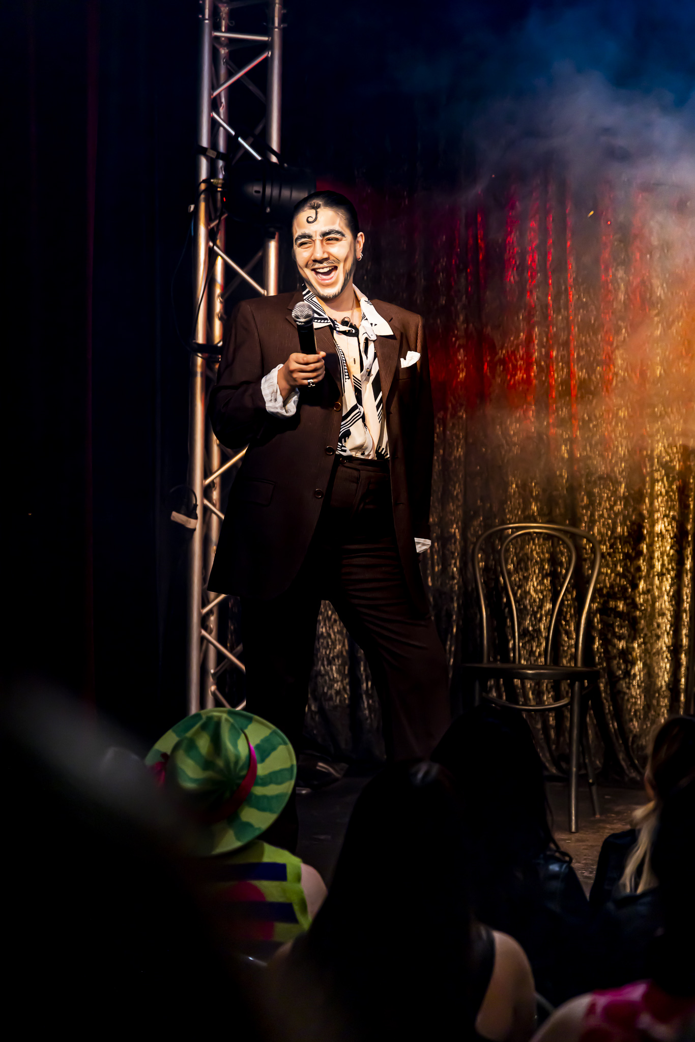 Bruno holding a mic while on stage, dressed in a suit and open neck shirt, in front of gold curtains