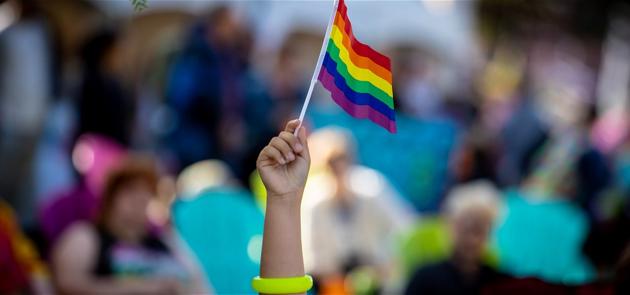 image of hand holding the pride flag, audience in background