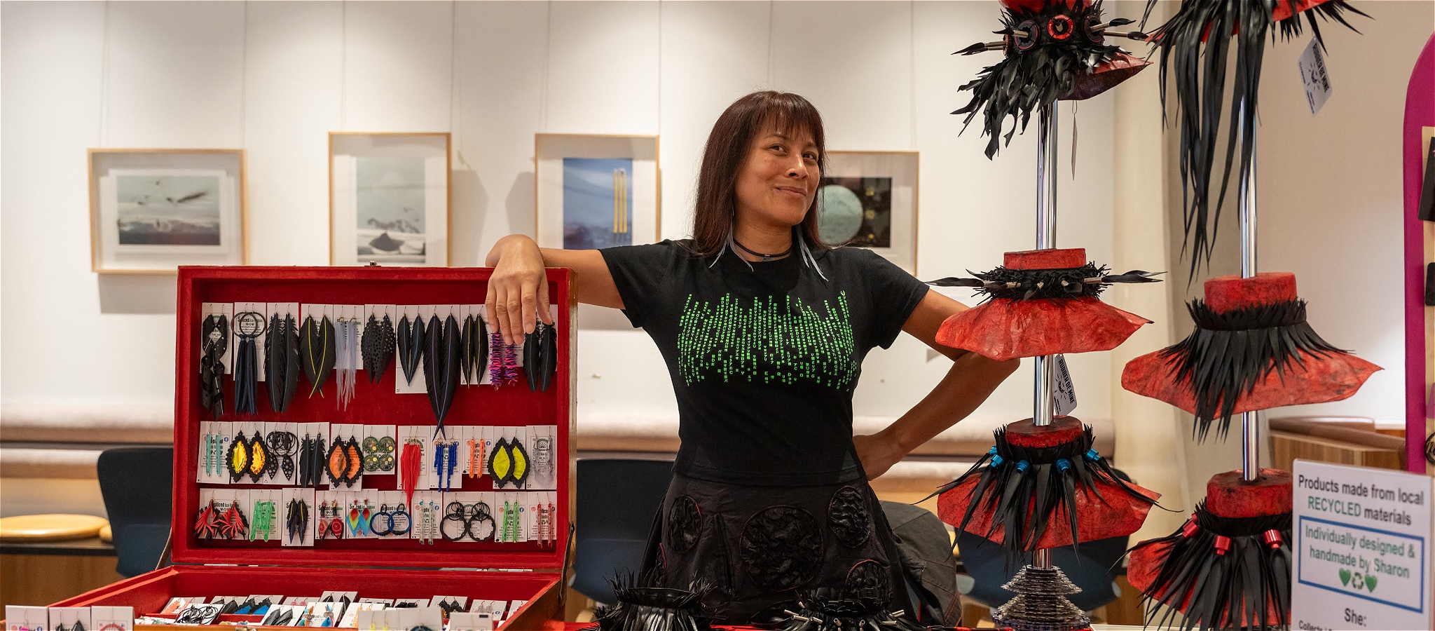 A woman stands proudly behind their market stall of feather neckwear, jewellery and recycled accessories.