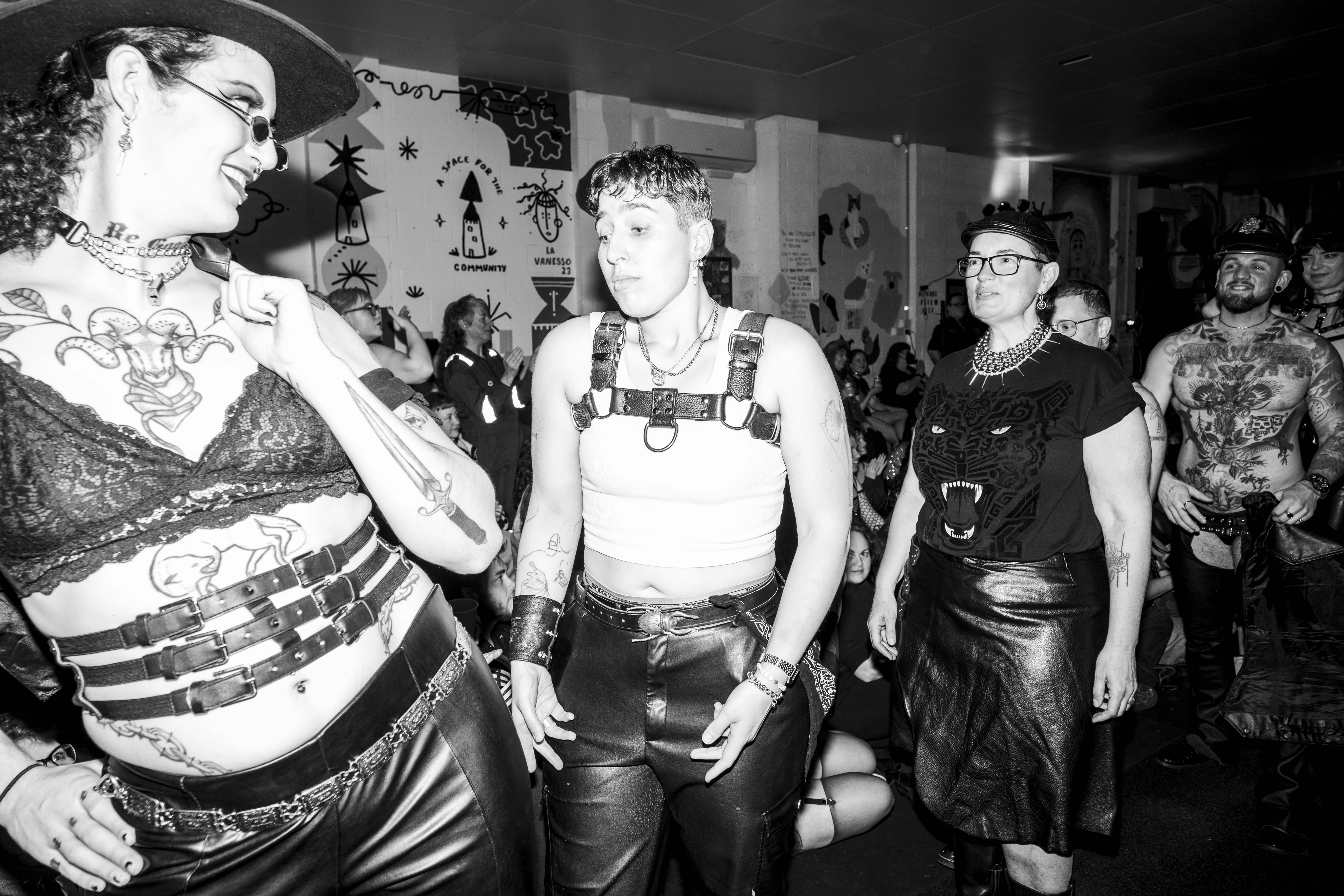 Black and white image of people walking on a catwalk. They have varying, dramatic expressions and some have tattoos.
