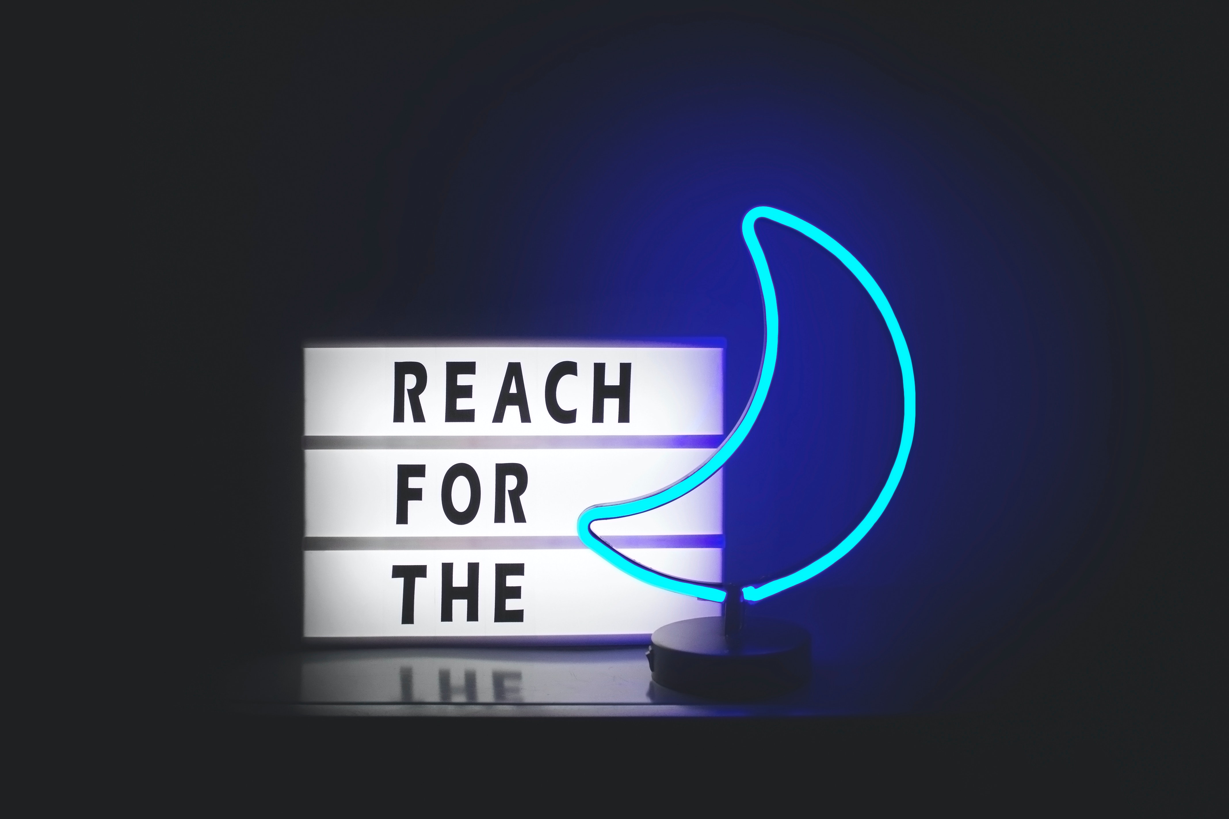 Sign reading 'REACH FOR THE' with a blue neon light in the form of a crescent moon
