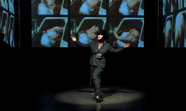 Person performing while dressed in black in front of dark images