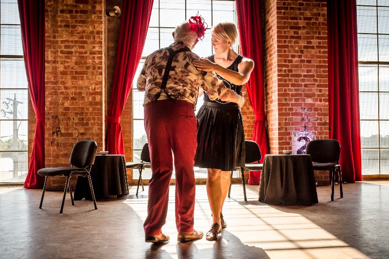 Two people doing ballroom dancing in a large sun-lit room with large windows
