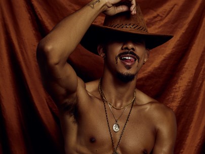Keiynan - bare chested, wearing black pants and holding their leather cowboy hat on their head