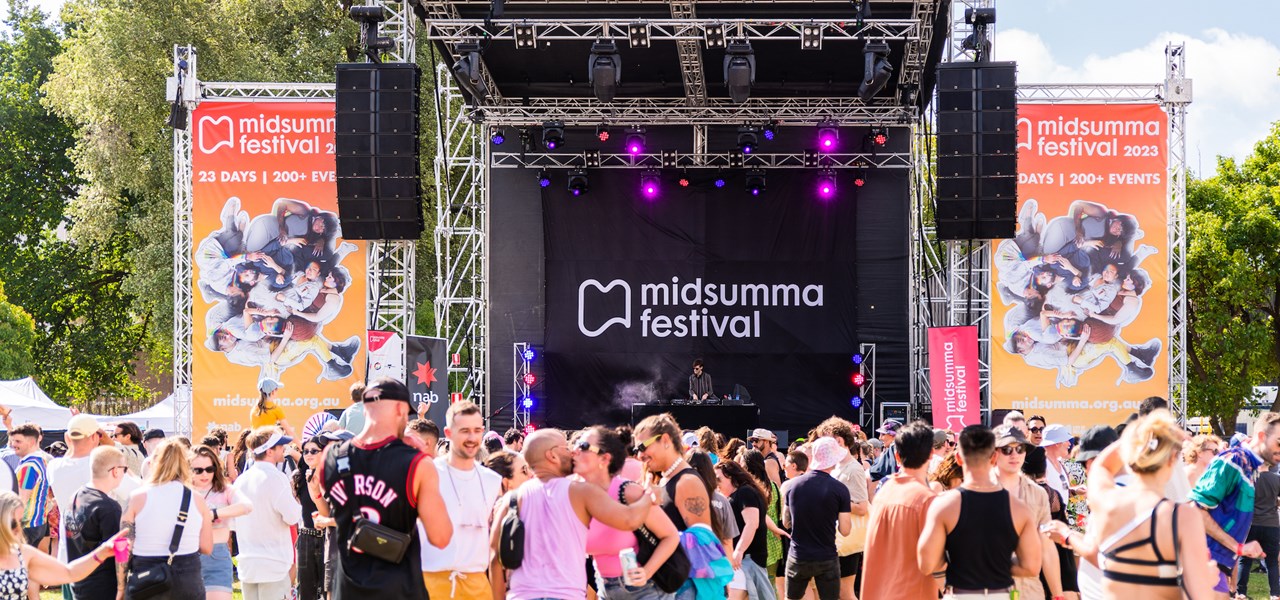 Midsumma Carnival Main stage with orange banners at the sides and a large crowd in the foreground