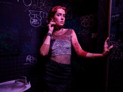 A person wearing a fish net top standing in a bathroom toilet in a night club.